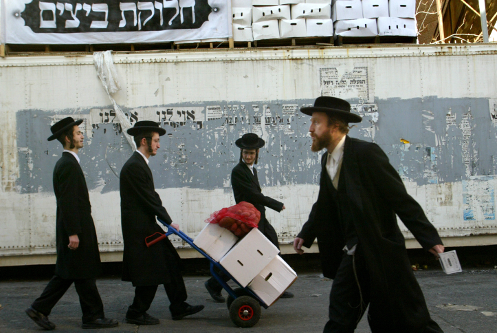 Ultra-Orthodox Jewish men leave as they cary food as another man holding a distribution ticket arrives to a food distribution point for people in need in advance of the high Jewish holiday of Passover